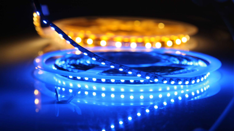 A close-up photo of coiled LED light strips glowing in blue and amber against a dark background.
