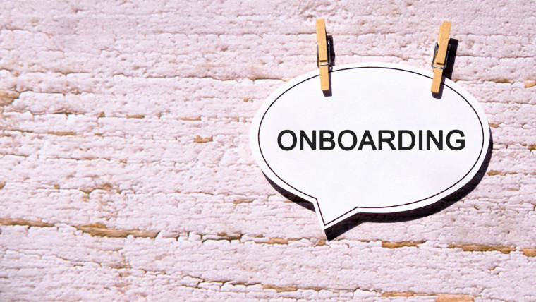 A paper speech bubble reading 'ONBOARDING' clipped to a textured wall with wooden clothespins.