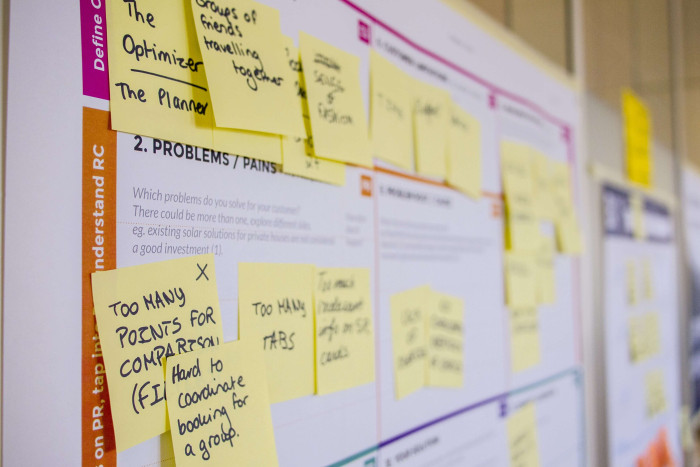 A photo of a product planning board covered in handwritten sticky notes, with a visible '2. Problems / Pains' section header and notes describing user pain points.