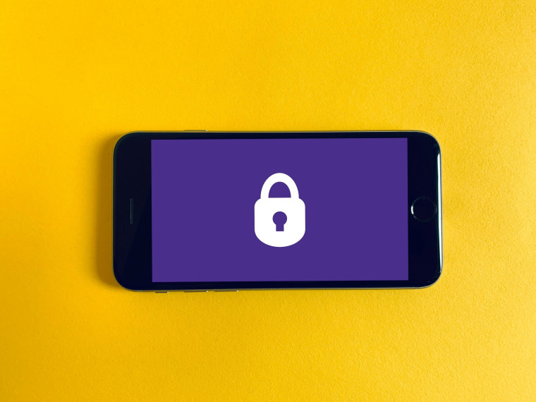 A smartphone lying on a yellow surface displaying a white padlock icon on a purple screen.