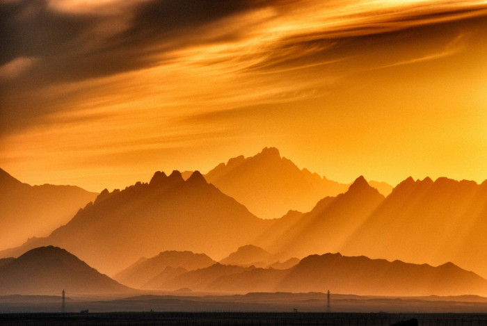 Mountain silhouettes in layers against a dramatic orange and amber sunset sky.
