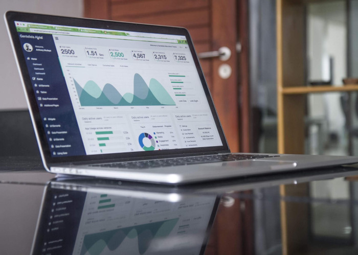 A laptop on a desk displaying an analytics dashboard with summary metrics, trend area charts, and usage breakdowns.
