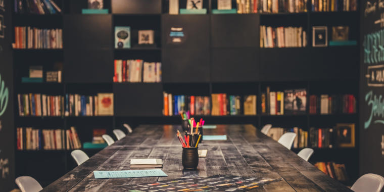A long wooden conference table in a room lined with floor-to-ceiling bookshelves.