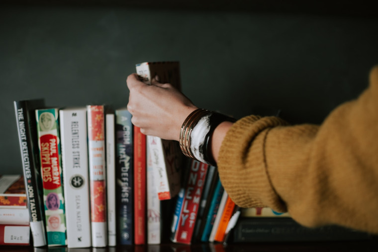 A hand reaching to pull a book from a shelf of books.