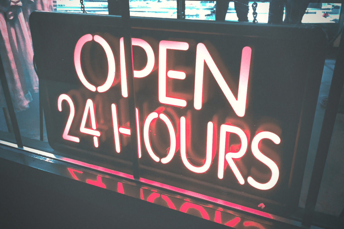 A neon 'Open 24 Hours' sign glowing in pink against a dark background