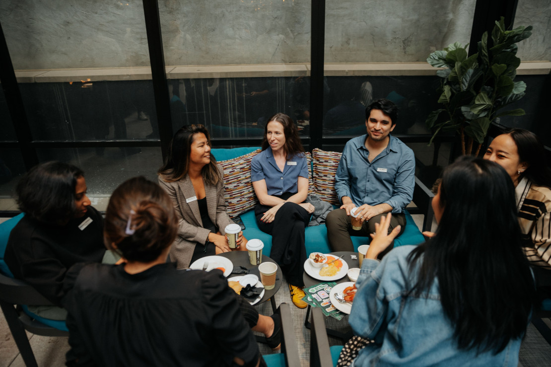 A group of attendees in conversation at a Chameleon in-person event, seated in a lounge setting with coffee and food.
